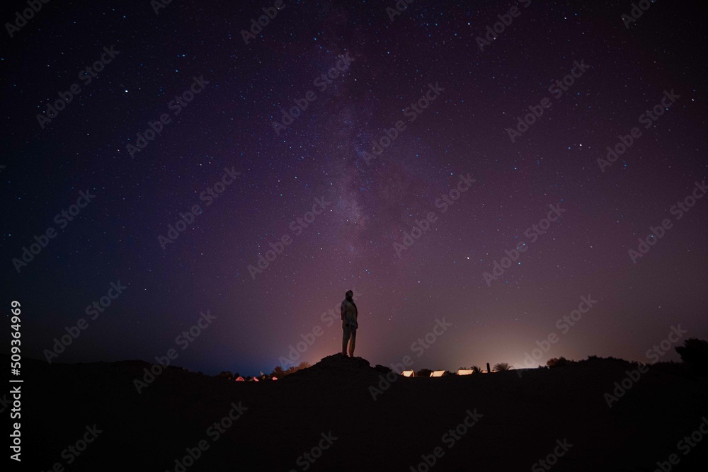 Fototapeta premium silhouette of a person standing on a rock looking at stars and milky way 