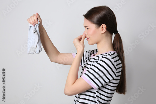 Young woman feeling bad smell from dirty socks on light grey background