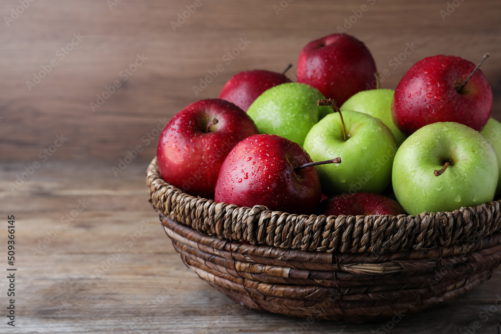 Fresh ripe green and red apples with water drops in wicker bowl on wooden table Fresh ripe green and red apples with water drops in wicker bowl on wooden table