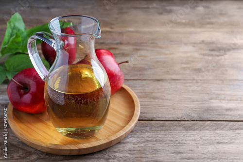 Jug of tasty juice and fresh red apples on wooden table, space for text photo