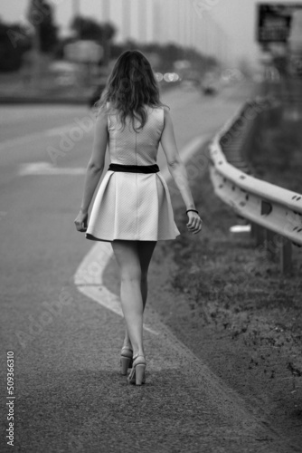 Slender woman walking by the road from back in black and white 