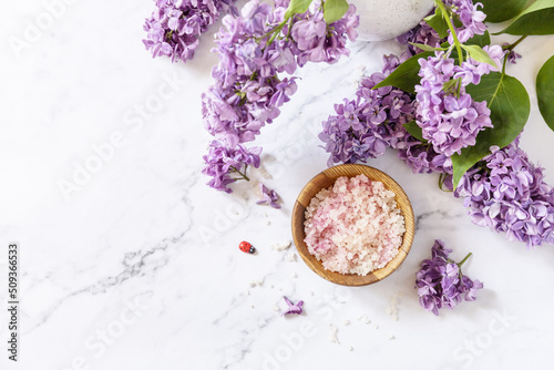 Spa setting. Organic spa sea salt and lilac flowers on a marble. View from above. Copy space.