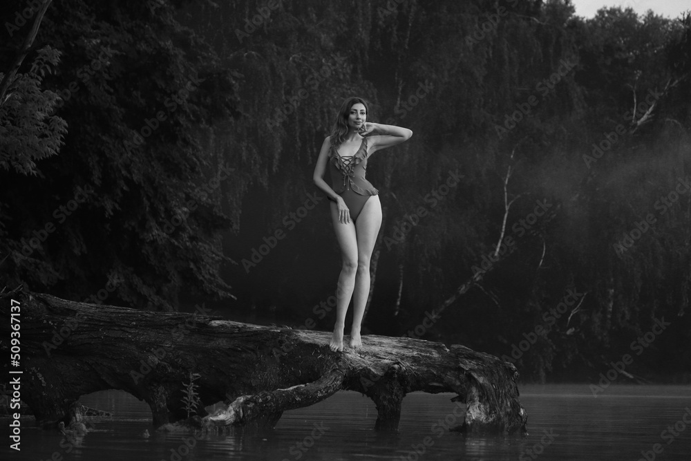 Beautiful woman in bikini on an old tree in the lake in black and white