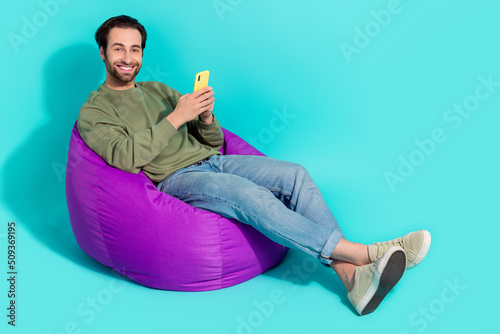 Full body profile side photo of young guy sit purple chair use mobile repost app isolated over turquoise color background
