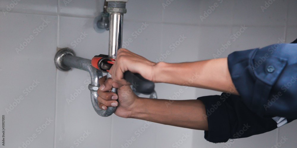 Male Plumber Using Wrench To Fix Leaking Sink In Home Bathroom. Male Plumber Using Wrench To Fix Leaking Sink In Home Bathroom.