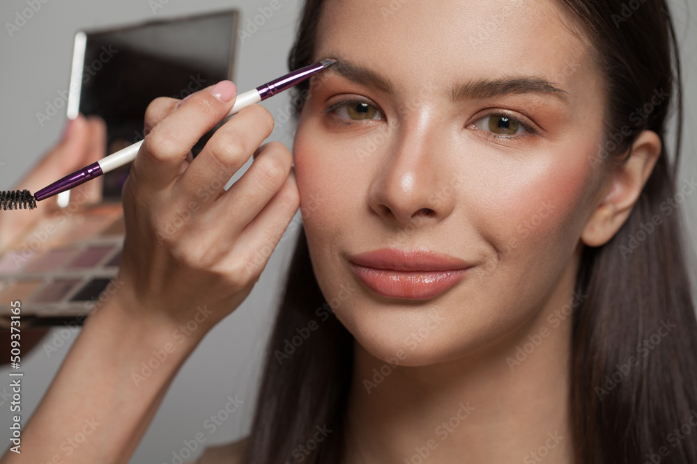 Makeup artist applies brown color shadow to a eyebrow of brunette woman. Make-up concept Makeup artist applies brown color shadow to a eyebrow of brunette woman. Make-up concept