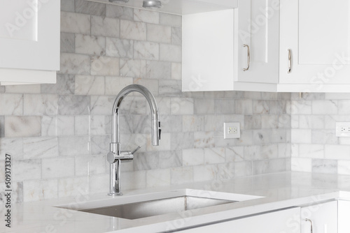A kitchen sink detail shot with white cabinets and a marble subway tile backsplash.