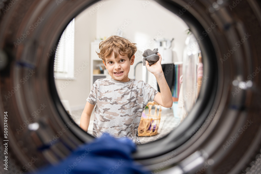 Shot from inside the washing machine view of the bathroom, laundry room. Little boy sits and throws socks aiming at drum, fooling around playing while cleaning. Shot from inside the washing machine view of the bathroom, laundry room. Little boy sits and throws socks aiming at drum, fooling around playing while cleaning.