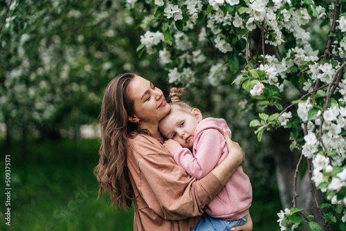 young mother with her daughter in her arms in a blooming apple orchard