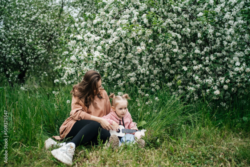 young mother and baby daughter play the ukulele in a blooming apple orchard in nature © Svetlana Repnitskaya