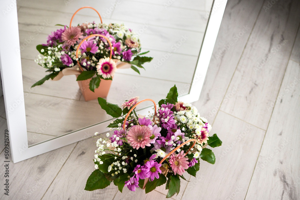 A composition of flowers in a festive box stands near the mirror and is reflected in it. A gift for a beloved woman A composition of flowers in a festive box stands near the mirror and is reflected in it. A gift for a beloved woman