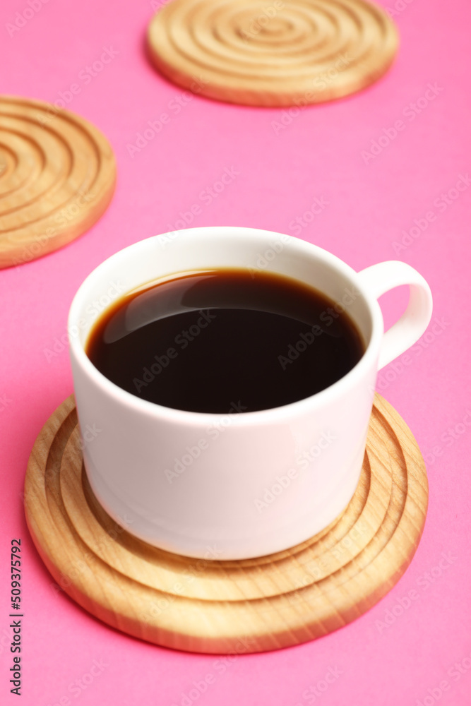 Obraz premium Cup of coffee and stylish wooden coaster on pink background, closeup