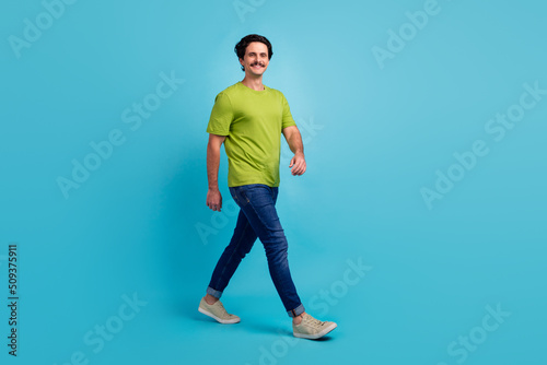 Full length photo of sweet positive man wear green t-shirt walking empty space smiling isolated blue color background