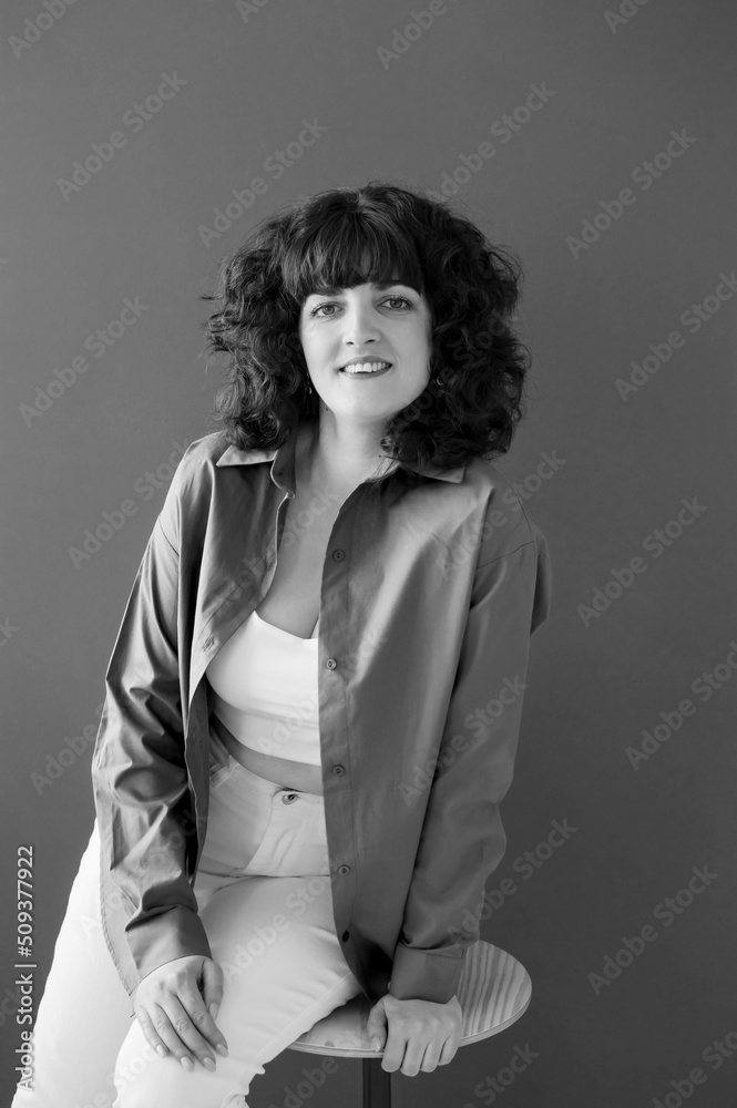 Happy girl with crooked teeth and cute with voluminous curly hair poses in background. An emotional, funny girl. Studio portrait. Concept of people's lifestyle. Vertical photo, black and white photo