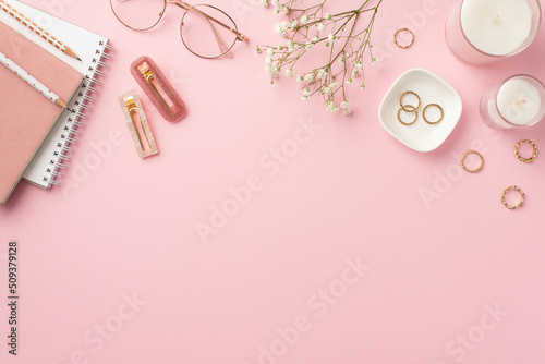 Business concept. Top view photo of workspace candles notebooks pencils stylish glasses gold rings trendy barrettes and white gypsophila flowers on isolated pastel pink background with copyspace