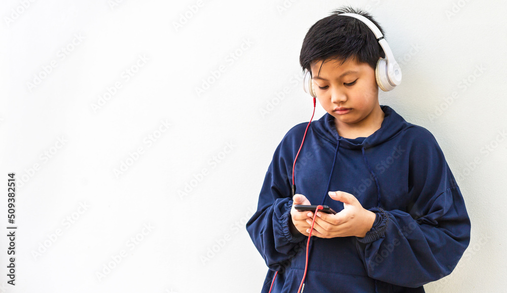 Cute Asian boy with white skin in a hoodie posing listening to the music on a mobile phone and headphones isolated over white background. portrait and copy space Cute Asian boy with white skin in a hoodie posing listening to the music on a mobile phone and headphones isolated over white background. portrait and copy space