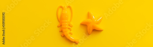 top view of starfish and shrimp toys on bright yellow background, banner.
