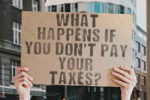 The question " What happens if you don’t pay your taxes? " is on a banner in men's hands with blurred background. Dollar. Draft. Negative. Rejection. Denial. Not. Poll. Refusal. Red. Duty. Facility © AndriiKoval