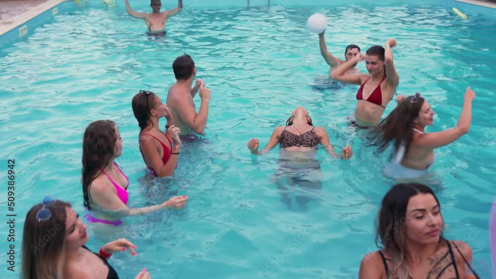 Friends have night pool party in a private villa swimming pool. Happy young people in swimwear splashing water, dancing with floaties and inflatable mattress in luxury resort. Friends have night pool party in a private villa swimming pool. Happy young people in swimwear splashing water, dancing with floaties and inflatable mattress in luxury resort.