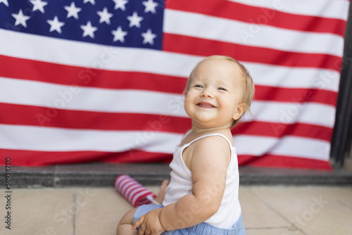 Patriotic holiday. Cute caucasian baby ten-eleven months old with blonde hair and blue eyes with American flag at home. USA celebrate independence day 4th of July.