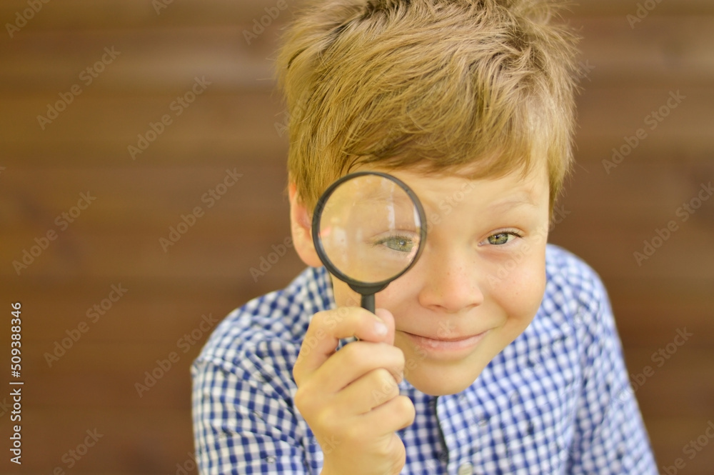 A schoolboy boy explores nature with a magnifying glass. Summer holidays for curious children in the forest. Hiking. Future scientist botanist A schoolboy boy explores nature with a magnifying glass. Summer holidays for curious children in the forest. Hiking. Future scientist botanist