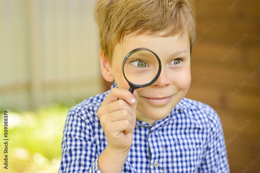 A schoolboy boy explores nature with a magnifying glass. Summer holidays for curious children in the forest. Hiking. Future scientist botanist A schoolboy boy explores nature with a magnifying glass. Summer holidays for curious children in the forest. Hiking. Future scientist botanist
