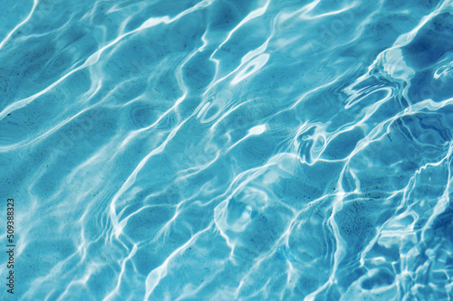 Blue water background of swimming pool or sea. Ripple water in swimming pool with sun reflection.