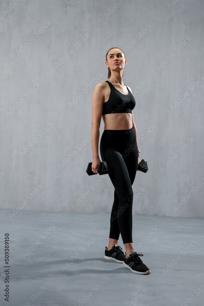 Athletic fitness woman working out with dumbbells on grey background. Copy space.