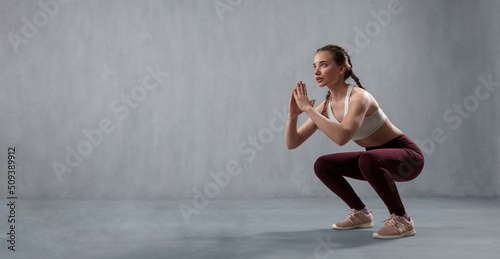 Sports woman in fashion sport clothes squatting doing sit-ups in gym, over gray background