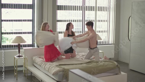 three friends have a pillow fight on bed - happy young threesome play together in hotel room photo