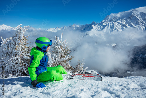 Ski boy sit looking on top of the mountain covered by clouds