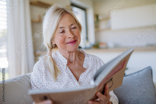 Senior woman sitting on sofa and reading book at home