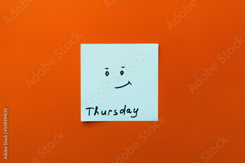 top view of sticky note with thursday inscription and positive smiley on orange background. photo