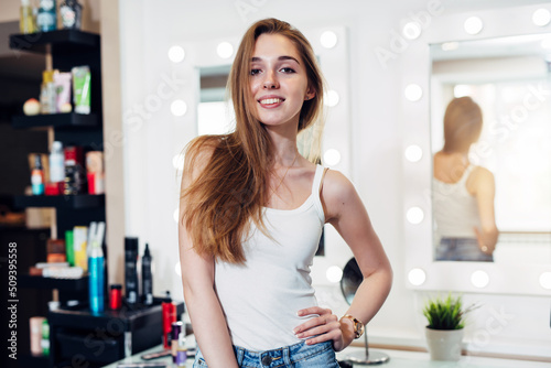 Portrait of pretty female beautician standing posing at workplace in hair and beauty salon