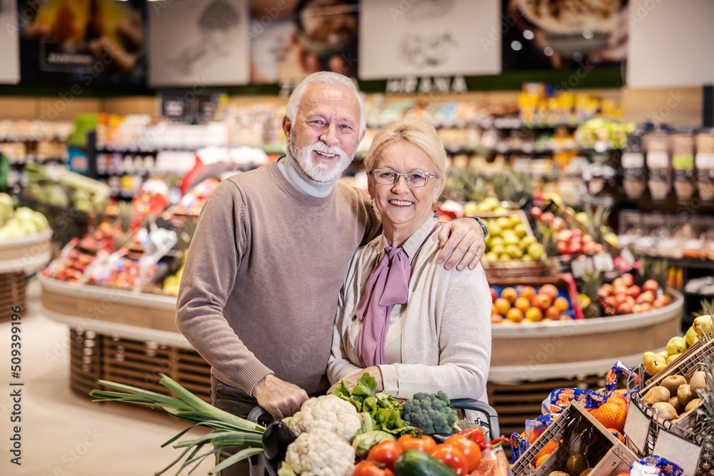 Senior couple hugging and shopping in supermarket while smiling at the camera.