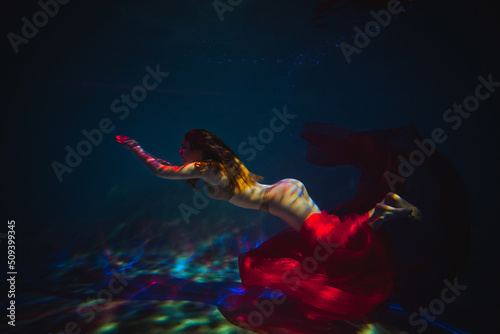 Art work. Underwater shot of a sports girl in lingerie with red material in the pool with beautiful highlights.