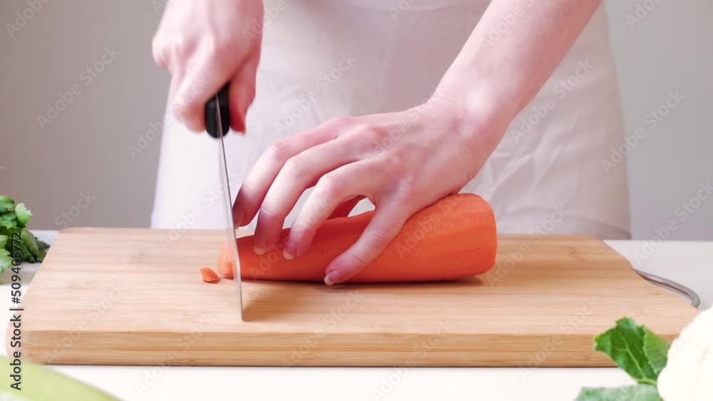Woman slices carrot into circles on a wooden cutting board on white table Woman slices carrot into circles on a wooden cutting board on white table