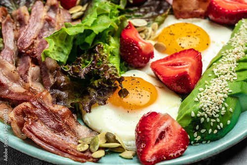 Fried egg bacon with avocado, strawberries and fresh salad. Delicious breakfast or lunch, Ketogenic, keto or paleo diet, Food recipe background. Close up