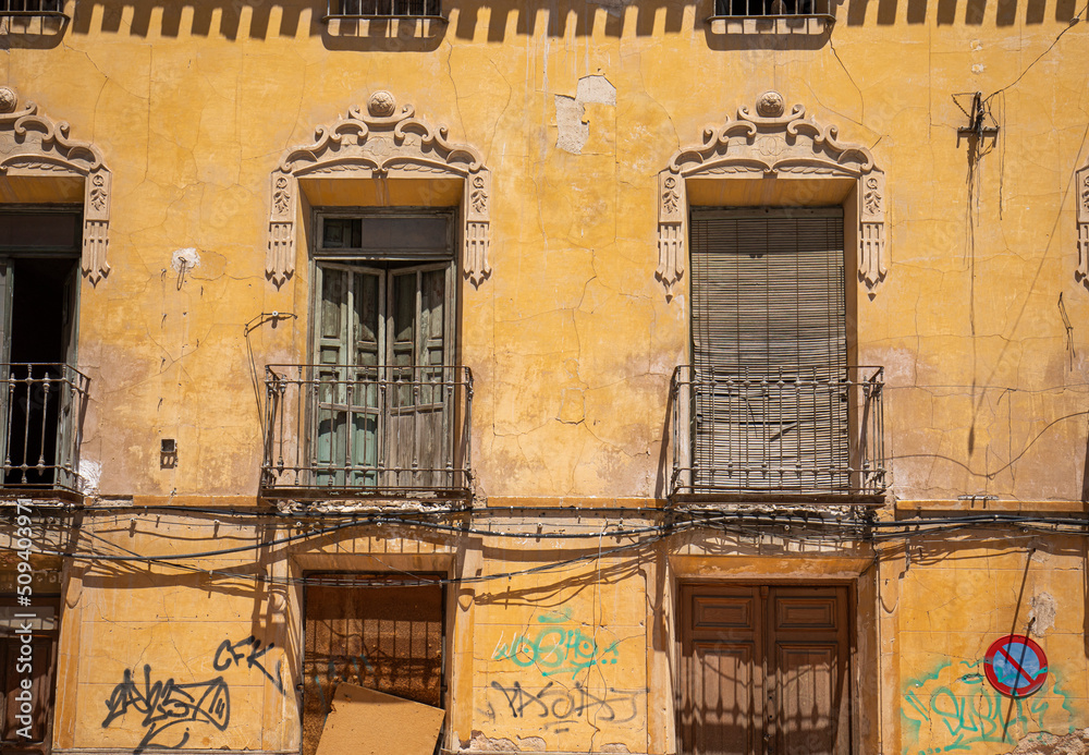 Facade of an old building with balconies and windows very deteriorated, with graffiti and cracks on the yellow facade