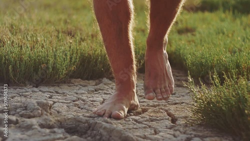 Man stepping barefoot from green grass to cracked soil ground photo