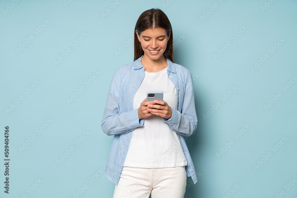 Pretty millennial woman using phone over blue copy space background holding phone in hands Pretty millennial woman using phone over blue copy space background holding phone in hands