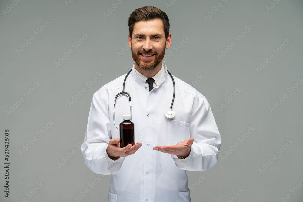 Waist up portrait view of the male doctor wearing white coat holding bottle with mixture and looking at the camera over grey background Waist up portrait view of the male doctor wearing white coat holding bottle with mixture and looking at the camera over grey background