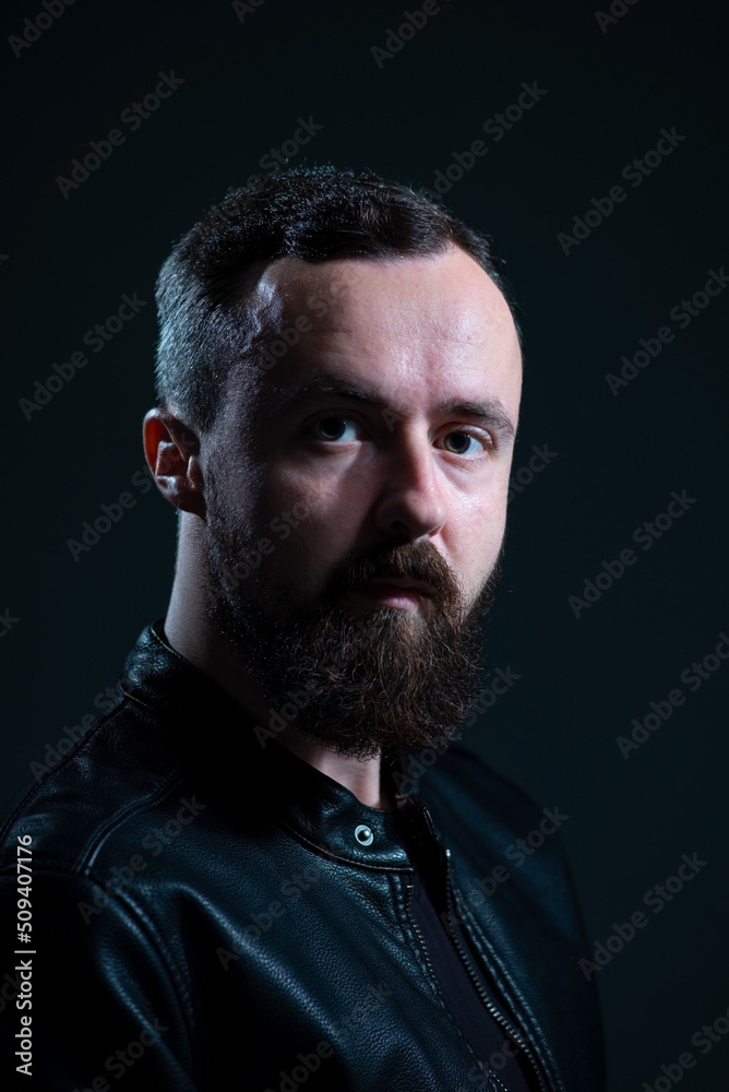 dramatic portrait of bearded millennial guy in leather jacket on dark background