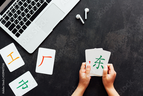 Flat lay mockup for online courses of Chinese language. Laptop and cards with basic printed characters on dark black concrete background with copy space. Inscription: work, middle, factory, east
