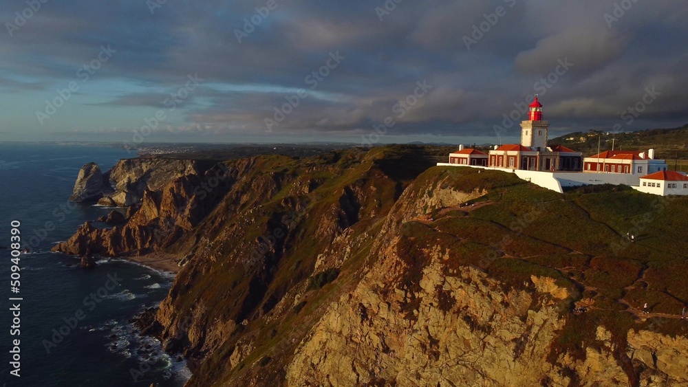 Drone flying around Cabo da Roca lighthouse located on a rocky cliff in the magic sunset light