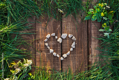 Top view of a table made of wooden planks, with a frame of green grass and a heart made of stones in the middle.