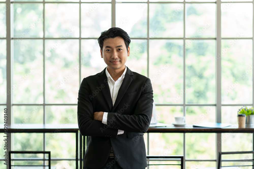 Portrait of Asian business man wear suit at the workspace office. Smiling Asian business man standing with arms crossed in background modern office Portrait of Asian business man wear suit at the workspace office. Smiling Asian business man standing with arms crossed in background modern office