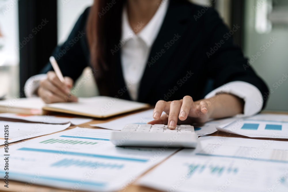 Close up of businessman or accountant hand holding pen working on calculator and laptop computer to calculate business data during make note at notepad, accountancy document at office Close up of businessman or accountant hand holding pen working on calculator and laptop computer to calculate business data during make note at notepad, accountancy document at office