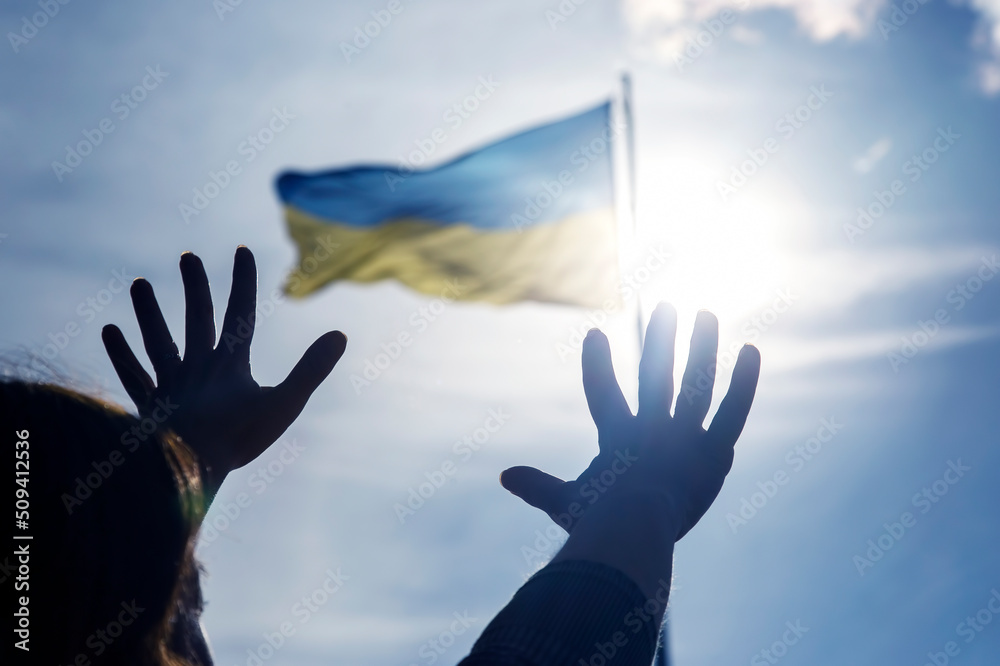 Raised hands to the sky against the background of the flag of Ukraine. Prayer for help and
