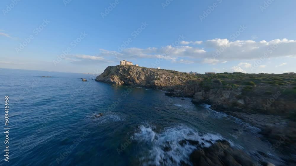FPV video, view from above, stunning aerial view from an FPV drone flying at high speed over a rocky coastline with a lighthouse illuminated during a dramatic sunset. Faro di Capo Ferro, Sardinia. FPV video, view from above, stunning aerial view from an FPV drone flying at high speed over a rocky coastline with a lighthouse illuminated during a dramatic sunset. Faro di Capo Ferro, Sardinia.